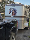 A silver horse trailer with a large horse graphic and the word 'RANCH' on the side, parked outdoors next to a black pickup truck on a gravel surface.