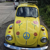 Yellow vintage car with peace sign and flower designs parked on a road.