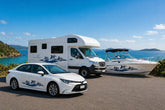 Mega Sticker Store dolphin stripe vinyl decals applied to a white car, motorhome, and boat by the coast.
