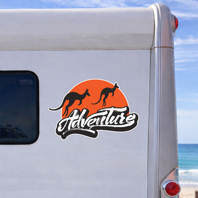 Back of a white camper van with 'Adventura' logo on a beach