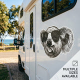 White RV with a koala sticker wearing sunglasses, set against a scenic background.