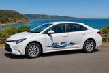 Mega Sticker Store dolphin and wave vinyl graphic decal applied to the side of a white sedan parked by the ocean.